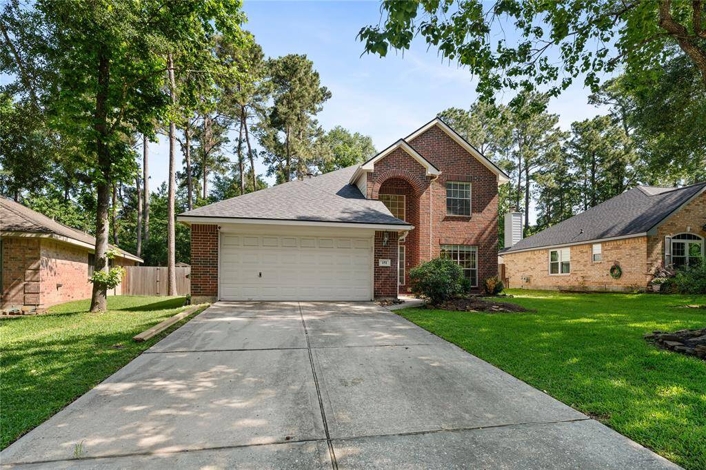 This photo showcases a charming two-story brick home with a well-maintained lawn and a two-car garage. The house is surrounded by mature trees, offering a sense of privacy and a natural setting.