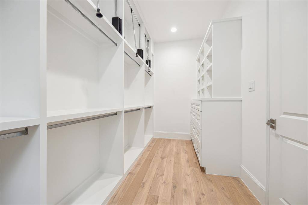 Spacious primary closet features built-in storage and ample room for hanging clothes with pull-down bars for accessing all custom storage solutions.