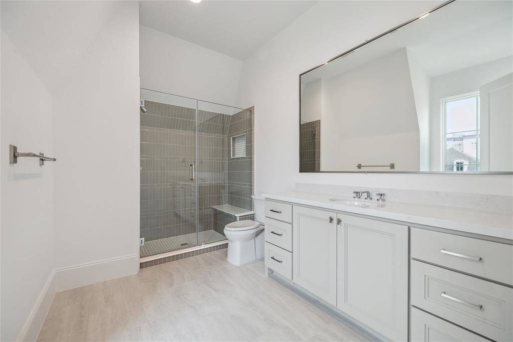 Oversized bathroom features glass-framed walk-in shower with niche, expansive mirror, and excess storage and counter space.