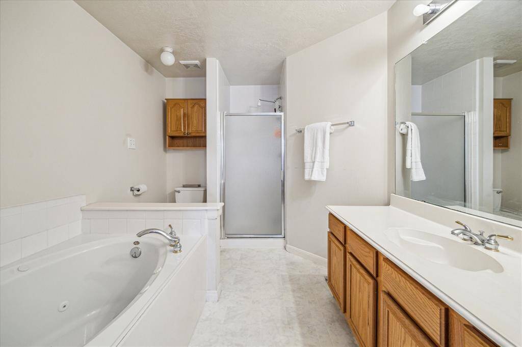This primary bathroom features a spacious layout with a large bathtub, a separate glass-enclosed shower, a wide vanity with ample storage, and a large mirror.