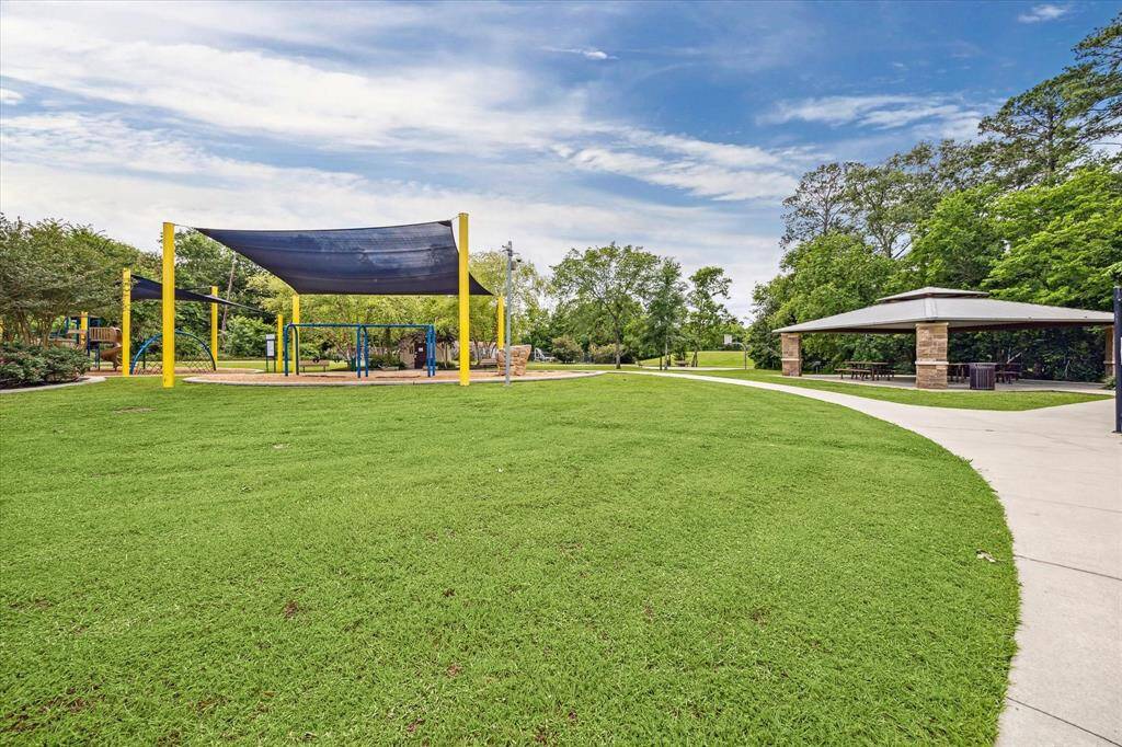 This photo showcases a spacious, well-maintained park with a playground featuring shaded areas, a pavilion with picnic tables, a splash pad and lush green lawns, ideal for family activities and relaxation.