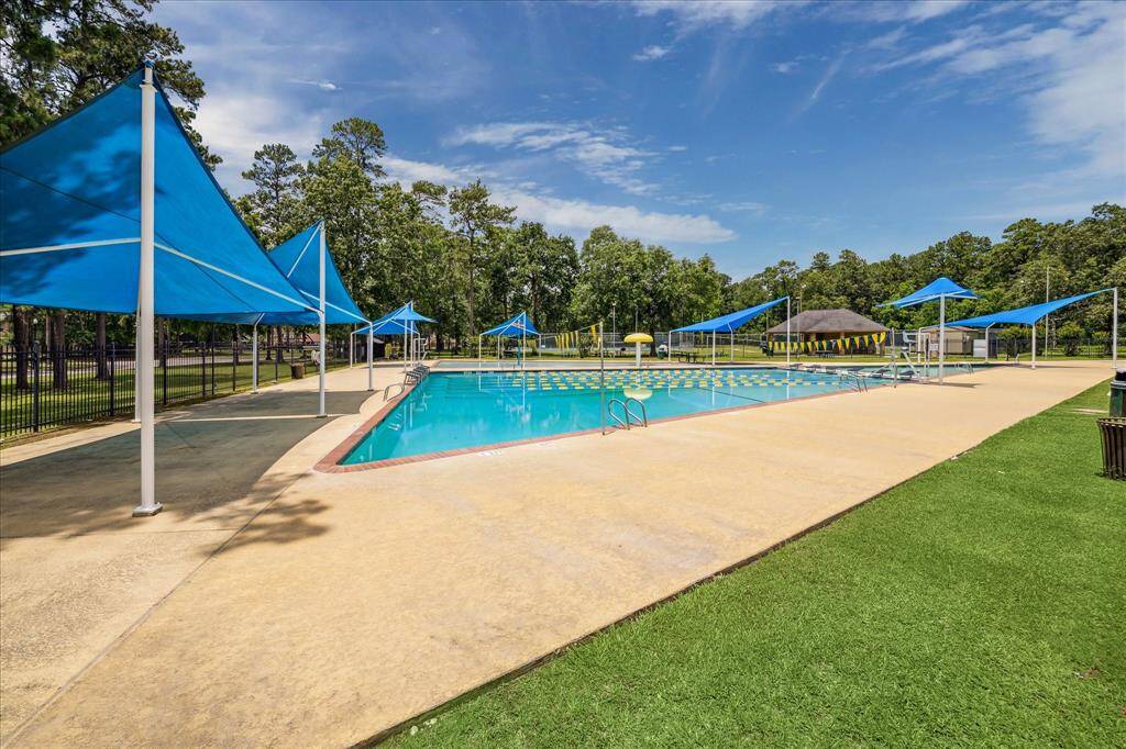 This photo showcases a spacious community pool with blue shade structures, surrounded by lush greenery, perfect for relaxation and family fun.