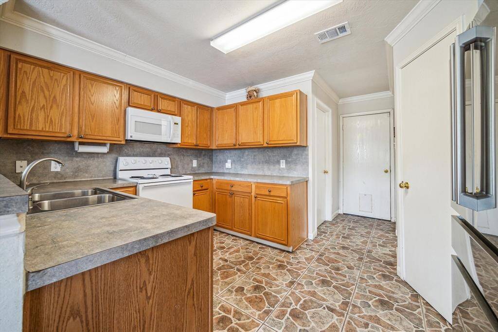 This kitchen features warm wooden cabinets, a spacious countertop. The patterned tile flooring adds character, while ample lighting and a neutral color palette create an inviting atmosphere.