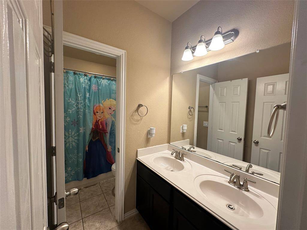 Secondary bath features tile flooring, dark stained cabinets, beautiful light countertops, mirror, double sinks, and sleek fixtures and modern finishes.