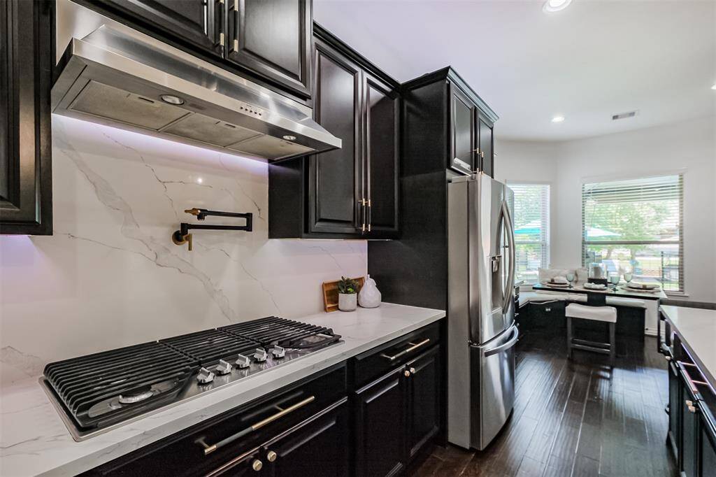 Note this fantastic Quartz backsplash with black and gold matte pot filler, 5 burner gas stove and the custom hardware on the cabinets.