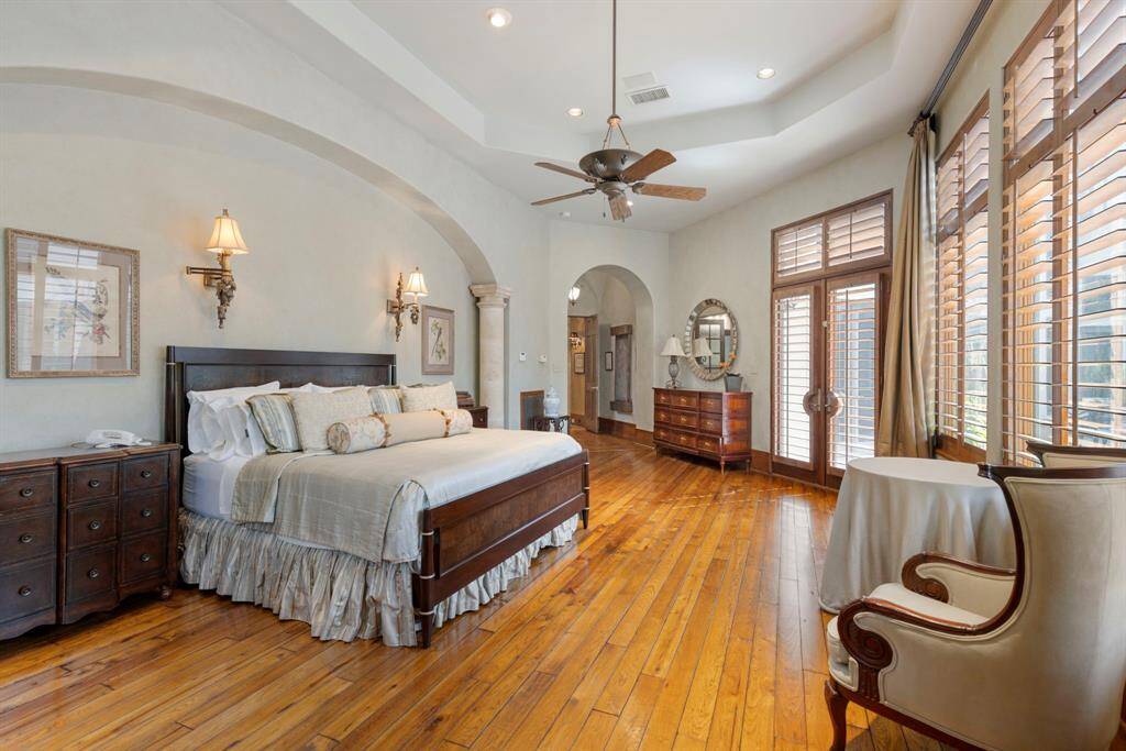 The primary retreat features warm wood floors, graceful arches, and timeless neutral walls, all beautifully complemented by a wall of windows and private access to the outdoor entertaining areas.