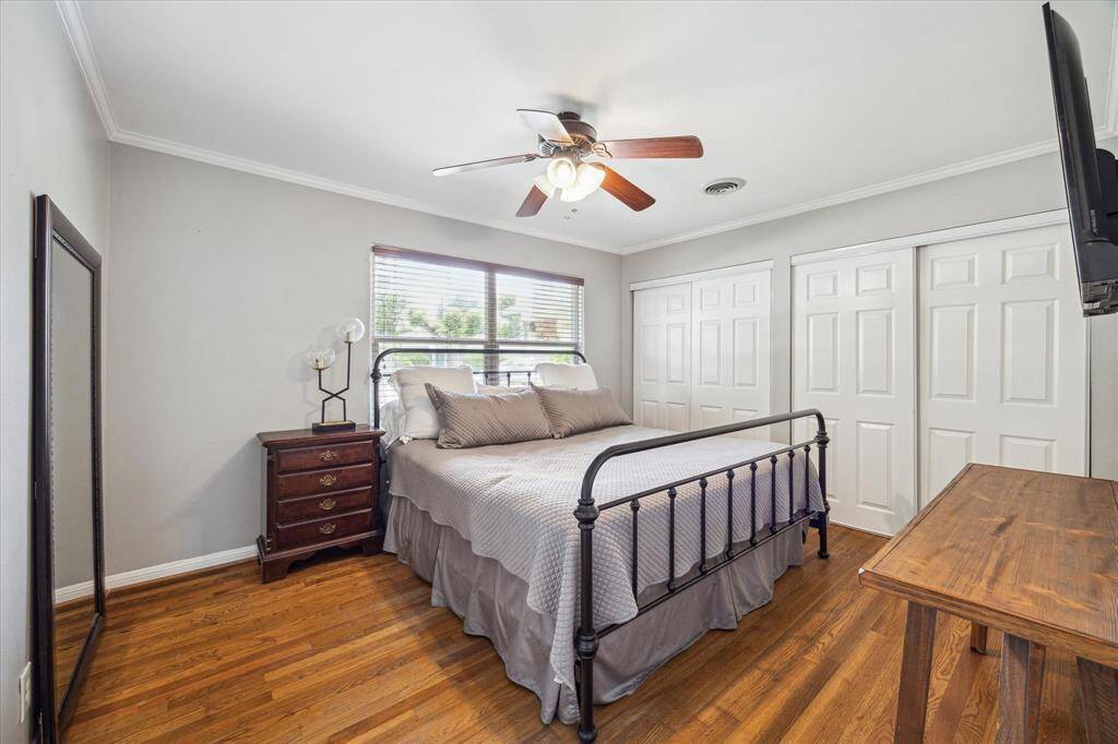 Double closets and a large window bring both functionality and natural light into the primary bedroom, grounded by warm wood floors and neutral tones.