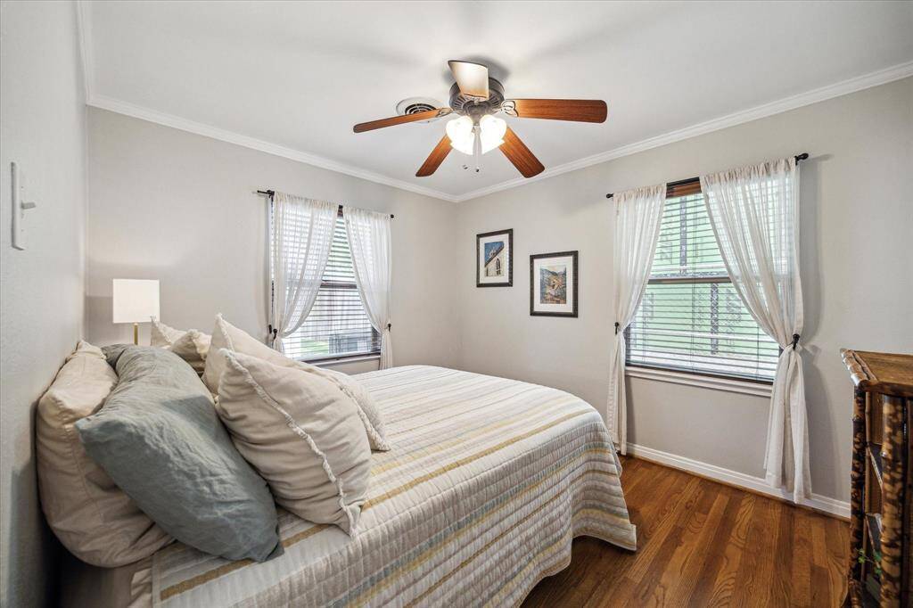 Soft natural light filters through sheer curtains in this inviting secondary bedroom. Hardwood floors add warmth underfoot, while neutral walls and crown molding enhance the clean, classic look. Dual windows offer peaceful backyard views and cross ventilation.