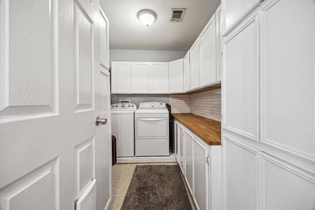Full-size washer and dryer are surrounded by generous cabinetry for storage and organization. Butcher block counters provide ample folding space, while a classic subway tile backsplash adds a timeless finish to this efficient laundry setup.