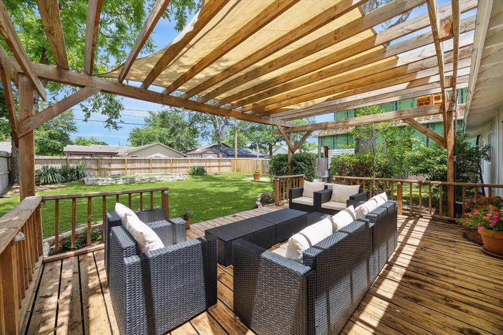 Wood-framed pergola casts dappled shade over the spacious deck, creating a relaxed retreat for morning coffee or weekend gatherings. Lush turf and a tiered garden bed define the backyard, while mature trees and privacy fencing complete the serene outdoor setting.