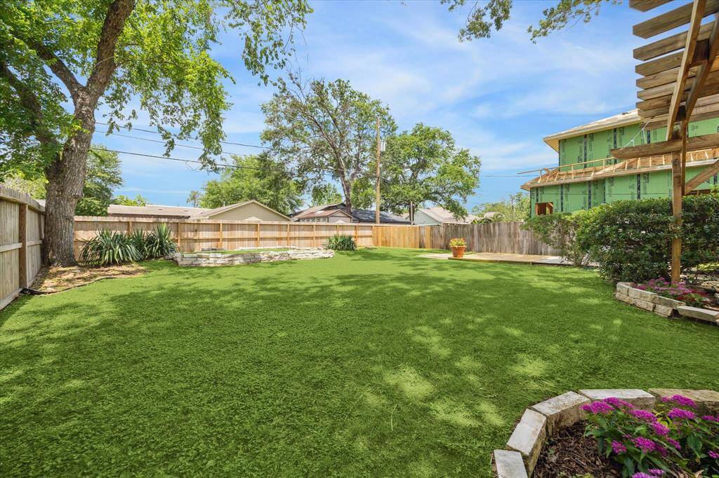 Sprawling backyard with lush grass, mature trees, and privacy fencing creates a natural escape with room to roam. Stone-edged flower beds and a raised planting area add texture and visual interest to the expansive green space.