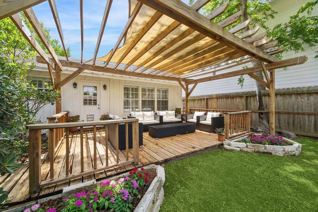 Fresh landscaping and vibrant blooms frame this inviting deck, where a wood-beamed pergola offers both shade and architectural interest. Thoughtful placement of outdoor seating turns the space into a seamless extension of the home's living area, perfect for quiet mornings or hosting friends.