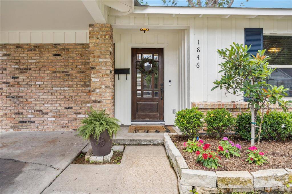 Brick and board-and-batten textures frame the inviting front door, accented by a warm wood finish and sidelights. A tidy front bed filled with colorful blooms adds a pop of charm, setting the tone for the thoughtful details found throughout the home.