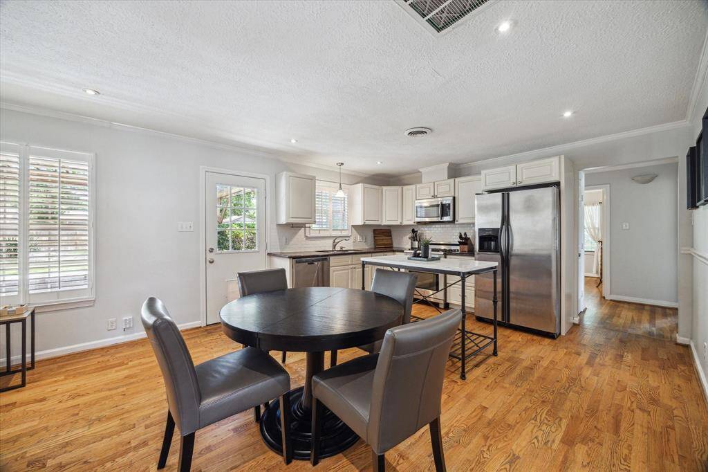 Open-concept kitchen and dining space features crisp white cabinetry, a classic subway tile backsplash, and stainless steel appliances, including a French door refrigerator. A central island offers extra prep space and seating, while natural light pours in through shuttered windows and a glass-paneled door that leads to the backyard.
