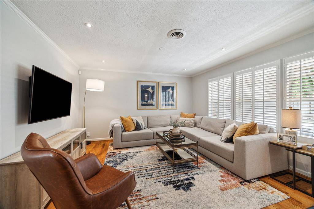 Wall of plantation shutters filters in soft daylight while offering privacy in this inviting living space. Neutral tones, hardwood flooring, and clean lines give the room a timeless and comfortable feel.
