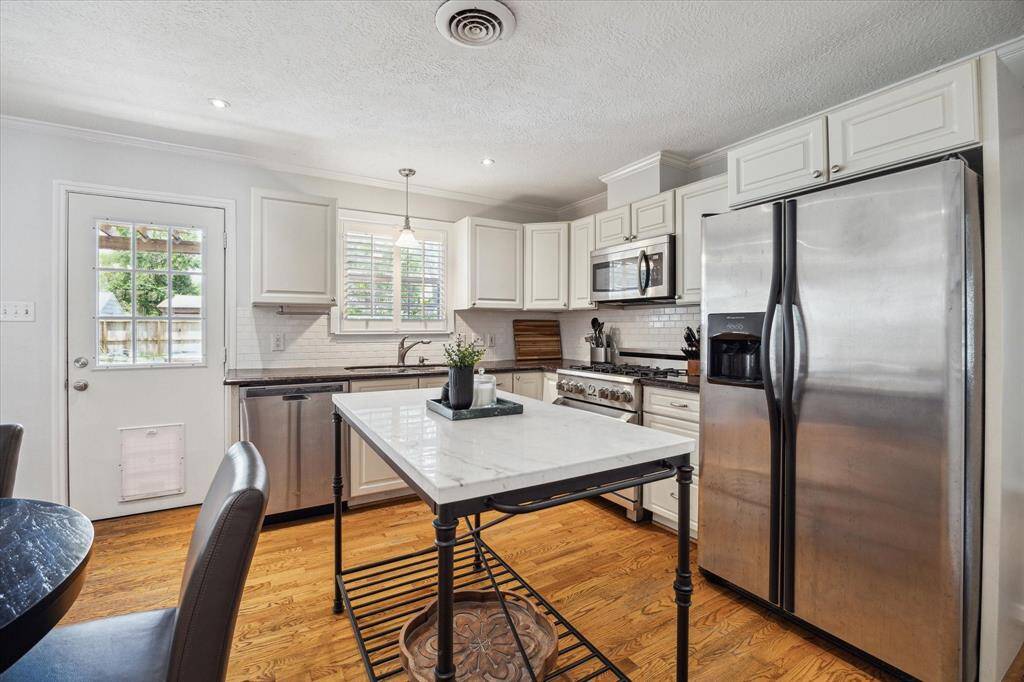 Natural light filters in through plantation shutters, illuminating the kitchen’s clean lines and stainless steel finishes. A marble-topped island adds both prep space and casual seating, while a pet door offers convenient backyard access.