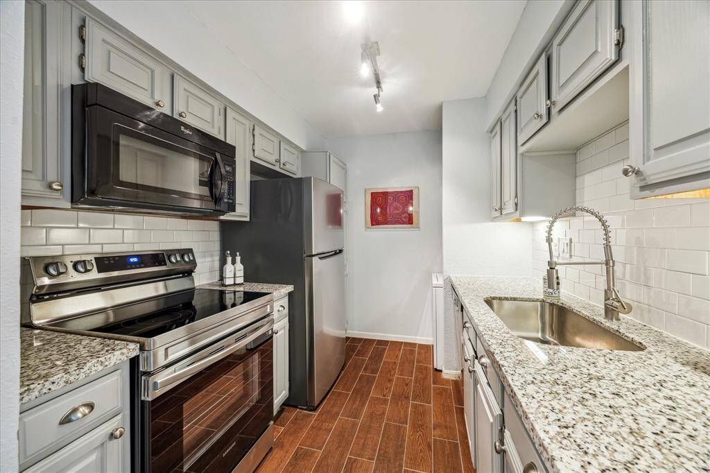 This galley kitchen packs a punch with gorgeous granite countertops, stylish tile backsplash with under-cabinet lighting, painted cabinetry with updated pulls, sleek stainless steel appliances, a deep basin sink with a pull-down fixture, and a floor-to-ceiling built-in pantry for maximum storage and organization.