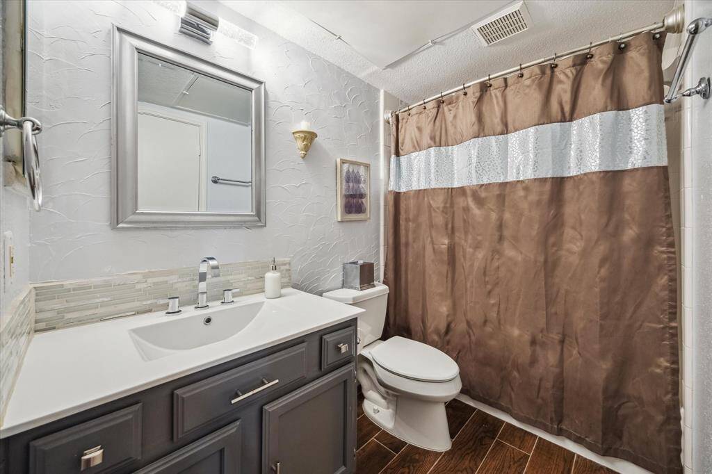 The full bathroom offers a cohesive blend of style and function, featuring an updated single-sink vanity with a solid surface top and smooth mount sink, paired with a framed mirror and sleek lighting above. A fully tiled tub/shower enclosure completes the space, providing both comfort and convenience for daily routines.