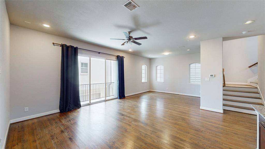 Spacious living area with hardwood floors, ceiling fan, and recessed lighting. Features large windows, sliding glass doors with balcony access, and a staircase leading to the 3rd floor.