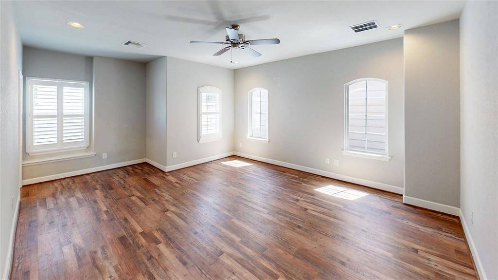 Located on the 3rd floor, this spacious Primary bedroom features warm Luxury Vinyl Plank floors, neutral walls, and ample natural light from multiple windows with shutters. It includes a ceiling fan and recessed lighting, creating a bright and inviting atmosphere.