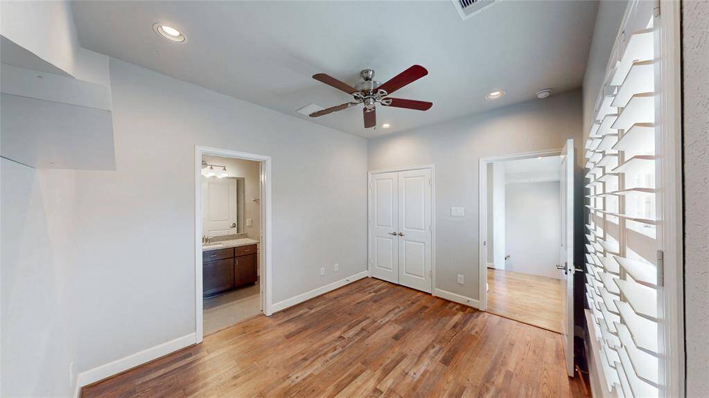 This room features Luxury Vinyl Plank floors, a ceiling fan, and recessed lighting. It includes a closet with double doors and an en-suite bathroom with a modern vanity. Shuttered windows provide natural light.