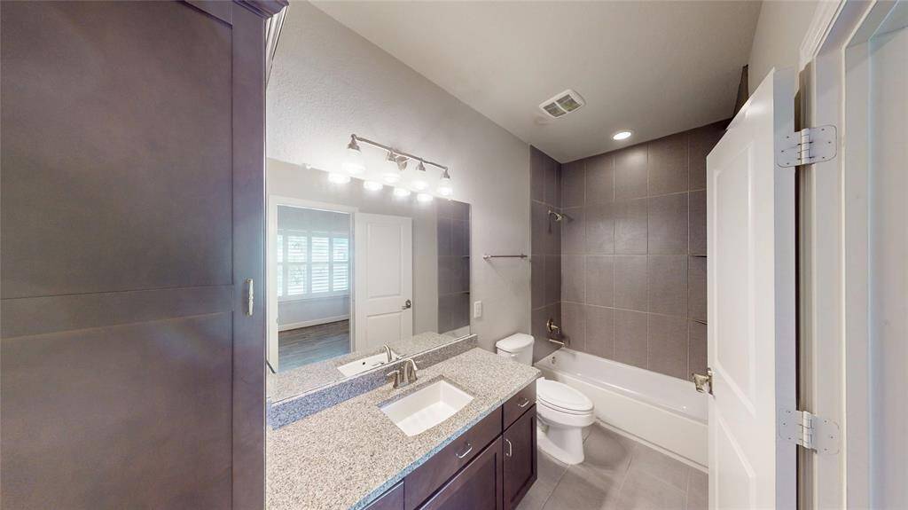 This modern bathroom features a sleek design with a granite countertop, under-mount sink, and dark cabinetry. It includes a bathtub with a tiled shower, bright lighting, and a neutral color palette, creating a clean and inviting space.