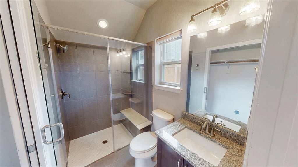 This bathroom features a modern design with a glass-enclosed shower, sleek gray tiles, and a granite countertop vanity. It offers abundant natural light and stylish fixtures, creating a bright and inviting space.