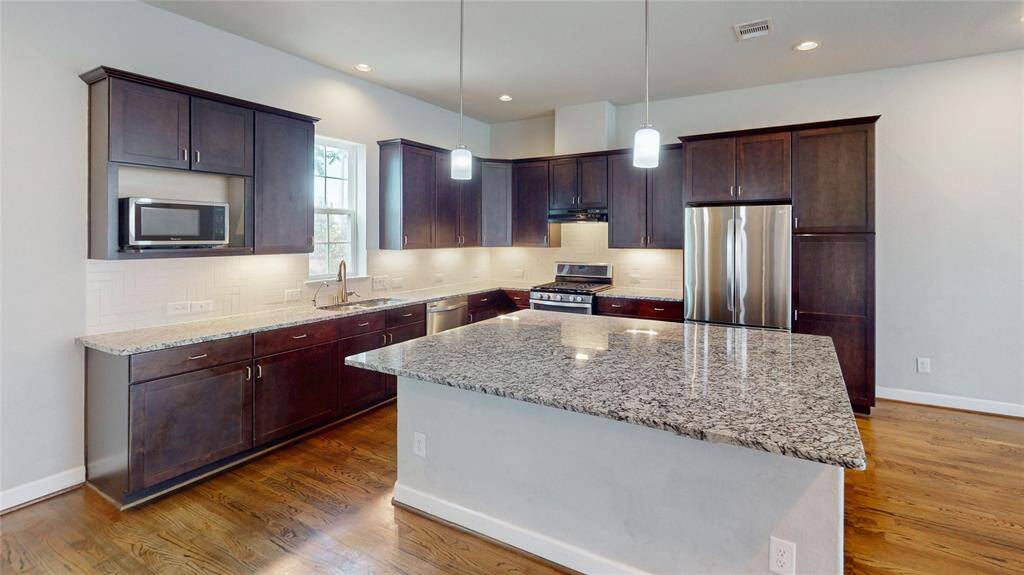 Located on the 2nd floor, this Modern kitchen features dark wood cabinets, granite countertops, stainless steel appliances, and a spacious island. Bright and inviting with hardwood floors and recessed lighting.