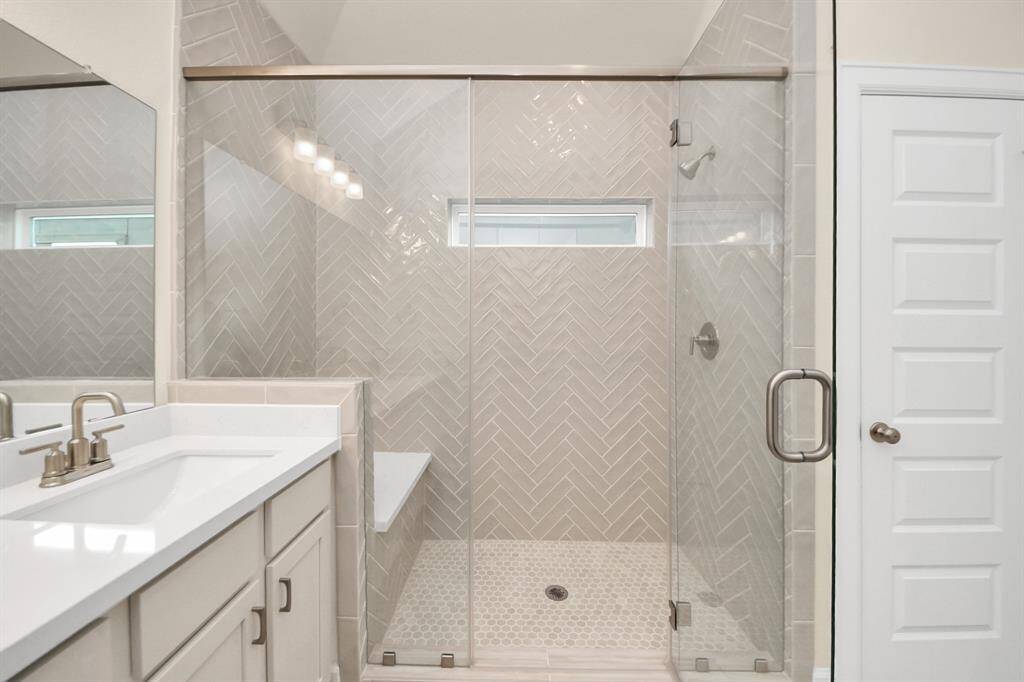 Close-Up: Luxury Walk-In Shower - A designer's dream—this frameless glass walk-in shower features a chic herringbone tile surround, built-in bench seating, and a soft neutral palette that adds both warmth and elegance. The sleek hardware and rainfall-style showerhead complete the spa-like feel. Benefits: Built-in bench for comfort and convenience; timeless herringbone tile adds elevated style and frameless glass = clean, open aesthetic.Every detail, beautifully finished.