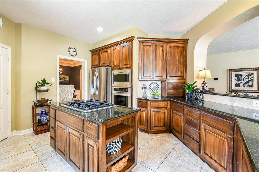The center island with 4-burner gas cooktop is ideally located near the refrigerator, oven, microwave, and sink!  Open shelving are perfect for displaying your cookbooks and other decor.   Note the appliance garage ahead on the right.  Perfect for storing those much needed but unsightly appliances we all have.