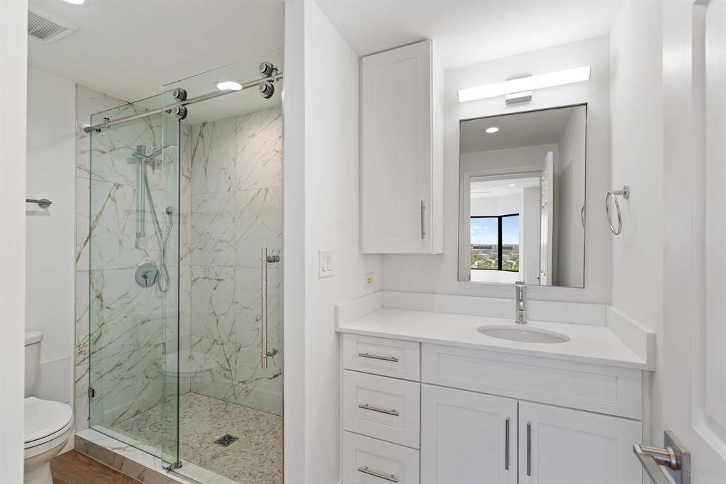 Primary bath with custom cabinetry, Quartz counters, sleek fixtures and seamless glass shower.