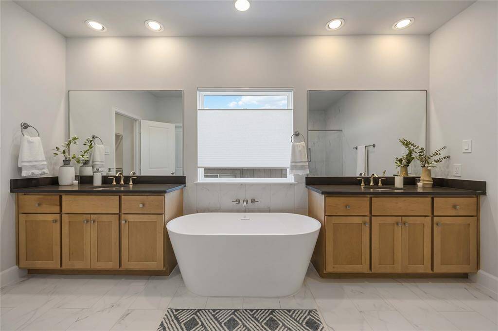 Step into primary ensuite bath with a vessel tub nestled between dual vanities, framed by custom wood cabinetry and sleek quartz countertops. Upgraded hardware throughout the home adds a luxurious touch, beautifully complemented by metal-framed mirrors.
