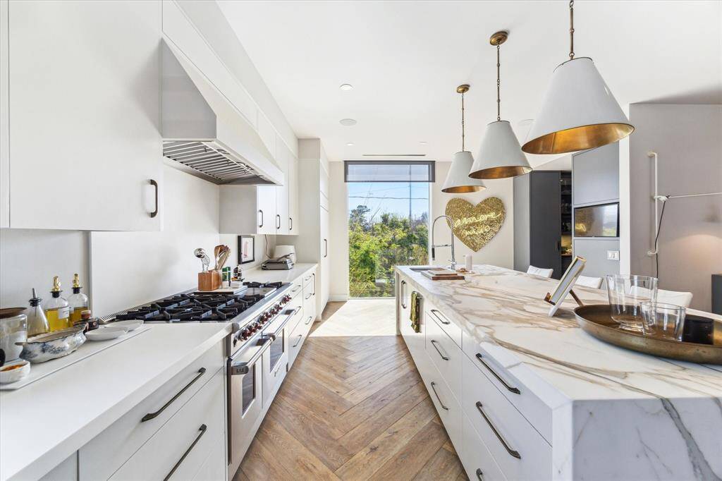 The kitchen at 2019 Du Barry, boasts a honed gold Carrara marble waterfall island, accentuated by Circa decorative lighting and seating for guests to chat, sip and relax in the heart of the home.