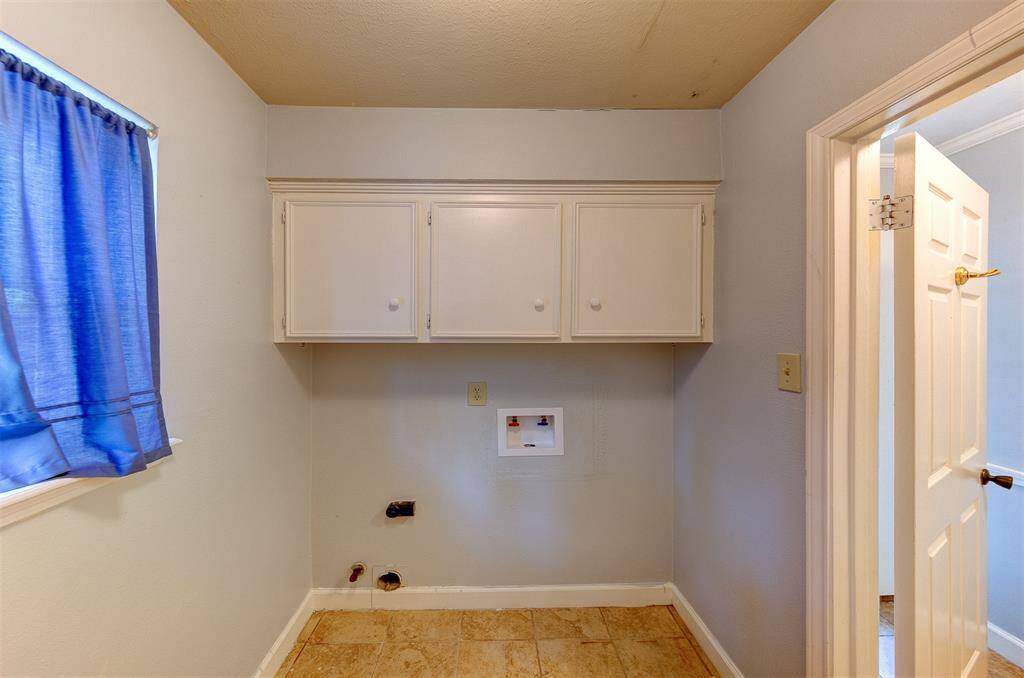 Spacious laundry room with shelves above units along with cabinets on the opposite wall.
