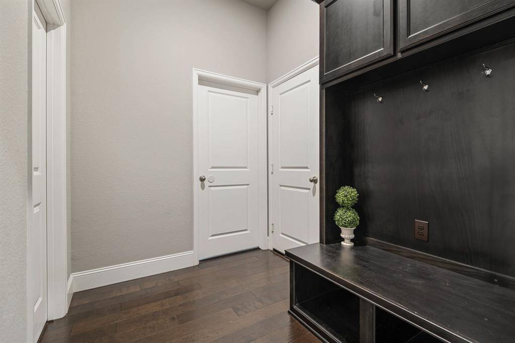 This photo features a hallway with dark hardwood floors and neutral walls. There's a built-in bench with storage and hooks, ideal for a mudroom setup. Garage door entry and Laundry Room door are featured in this photo and add to the clean and modern aesthetic.