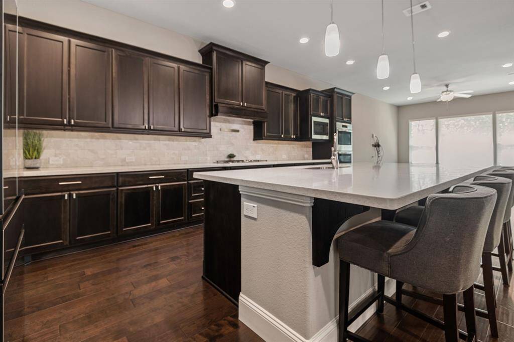 This modern kitchen features dark wood cabinetry, a large center island with seating, pendant lighting, and stainless steel appliances, offering a spacious and stylish cooking and dining area.