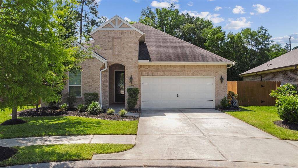 Charming single-story brick home with a two-car garage, lush green lawn, and mature trees providing ample shade. The property features a well-maintained garden and a welcoming pathway leading to the entrance. Homes have sidewalk