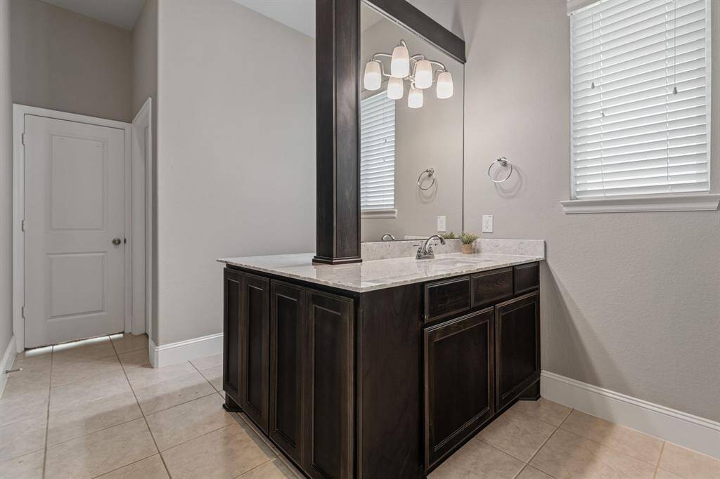 This bathroom features a sleek His & Hers vanity with dark wood cabinetry, a large dual mirror, and modern lighting. The space is brightened by a window with blinds, and the neutral tile flooring complements the neutral wall tones.