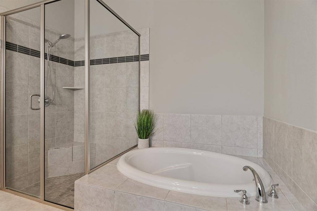 Modern bathroom featuring a spacious glass-enclosed shower and a separate oval garden tub, accented with neutral tiles and a sleek faucet.