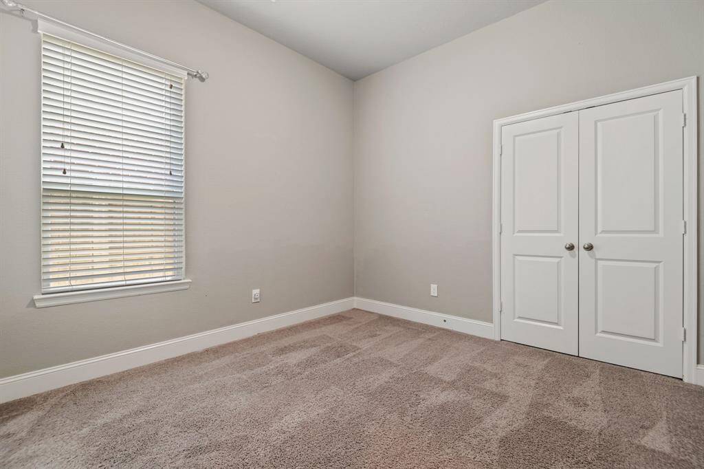 Secondary Bedroom 2 features neutral walls, plush carpet, a window with blinds for natural light, ceiling fan, and a double-door closet, offering a cozy and functional space.