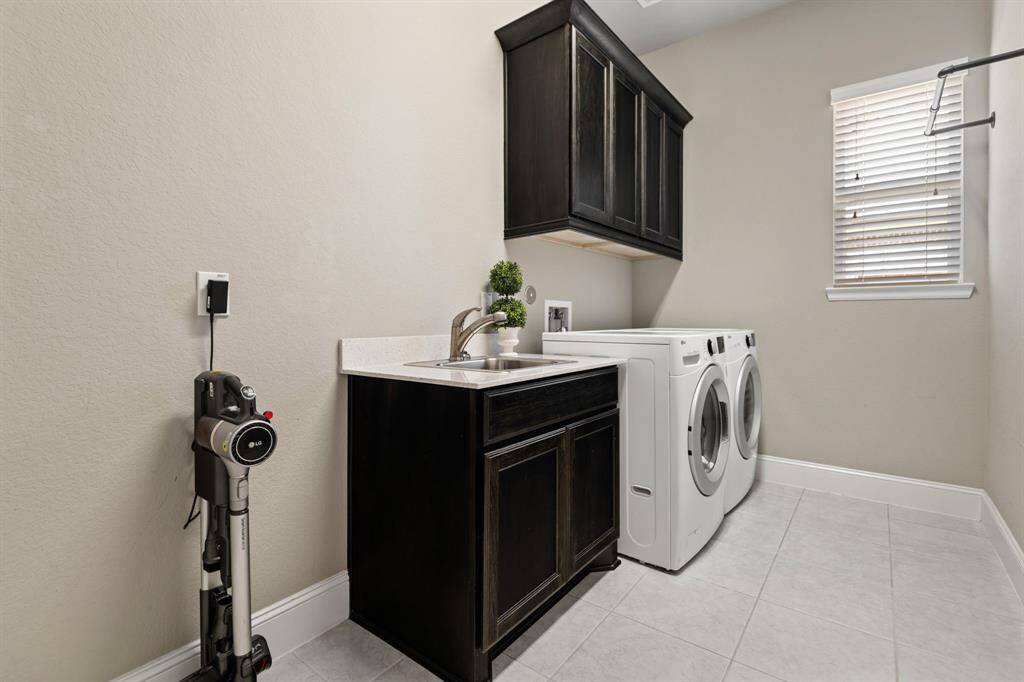This laundry room features modern appliances, a sleek sink with dark cabinetry, and ample natural light, blinds and even room for a fridge/freezer. It's efficiently designed for both functionality and style.