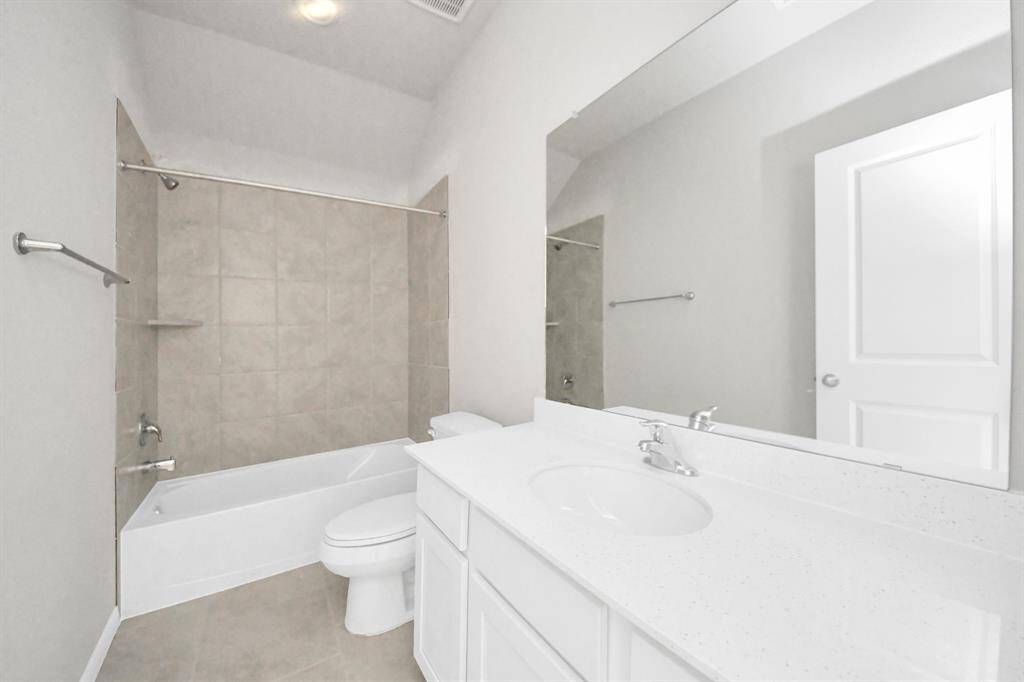 Secondary bath features tile flooring, bath/shower combo with tile surround, light stained wood cabinets, beautiful light countertop.