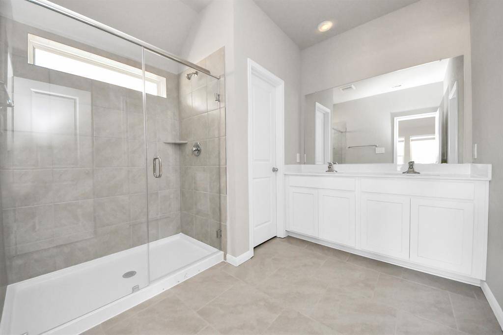 Experience luxury in this spa-like primary bathroom featuring a massive walk-in shower with tile surround. Light colored cabinets with light granite countertops complement the space, alongside a spacious walk-in closet with shelving, high ceilings, custom paint, and sleek, dark modern finishes. An ideal retreat for unwinding after a long day!