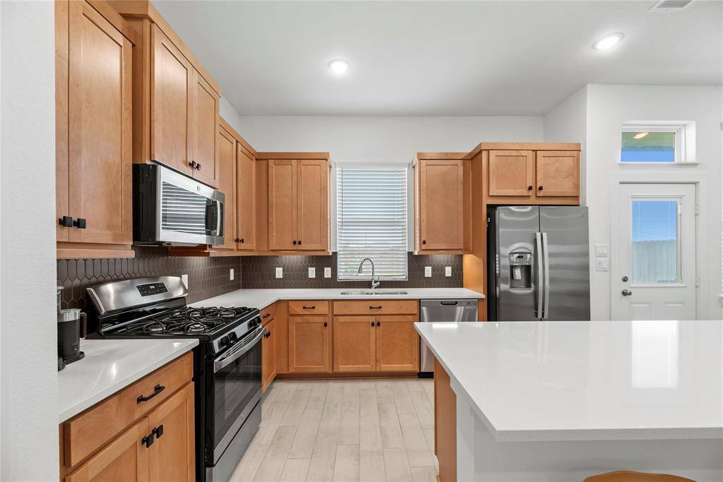 Beautiful cabinetry, under cabinet lighting, tile backsplash, Quartz countertops, stainless steel appliances, gas range and window above the sink with backyard views.