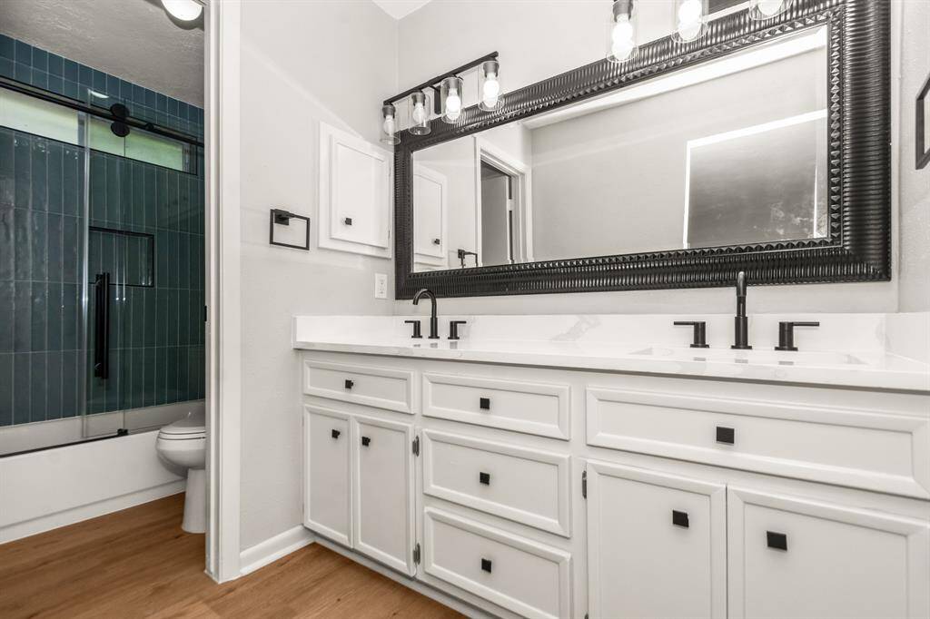 Updated primary bath with new glossy sage ceramic tile, new toilet, new designer glass enclosure, new faucets, new lighting, new counters, and new hardware all in a modern and clean aesthetic.