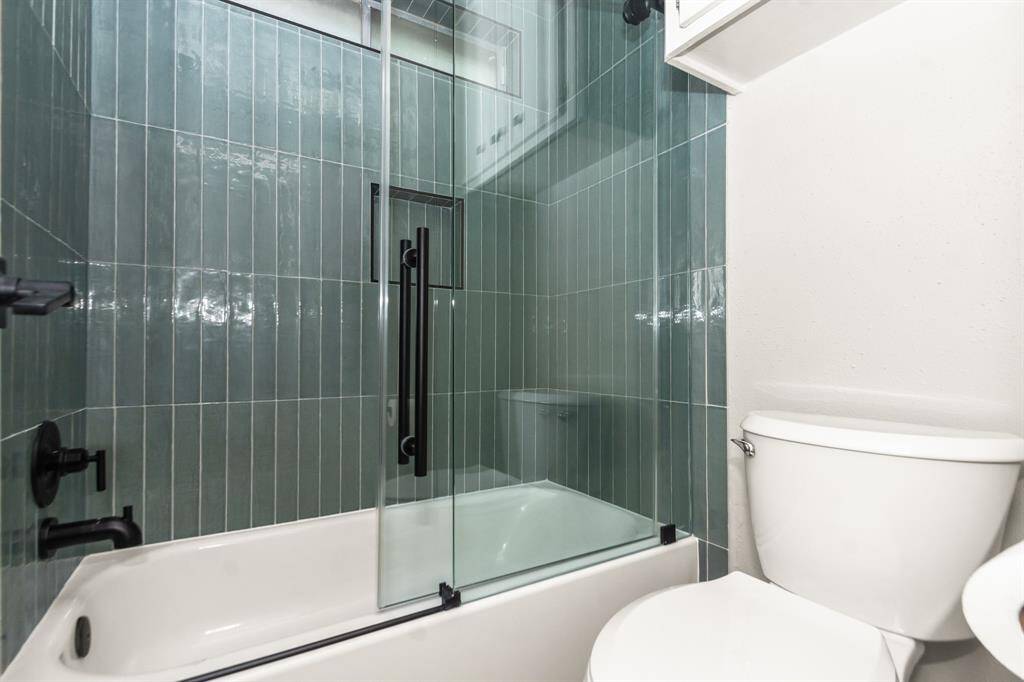 The updated primary bathroom showcases elegant glossy sage ceramic tile, a sleek frameless glass shower door, and stylish new tub hardware