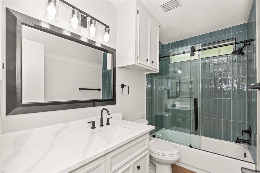 Stylishly renovated hall bath with matching sage ceramic tile, updated fixtures, and a quartz countertop.