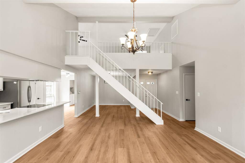 The living room impresses with soaring 16-foot ceilings, a sleek metal staircase, and brand new rich wood-look LVP flooring. Open sightlines extend into the updated kitchen, creating a bright and connected living space perfect for everyday living and entertaining.