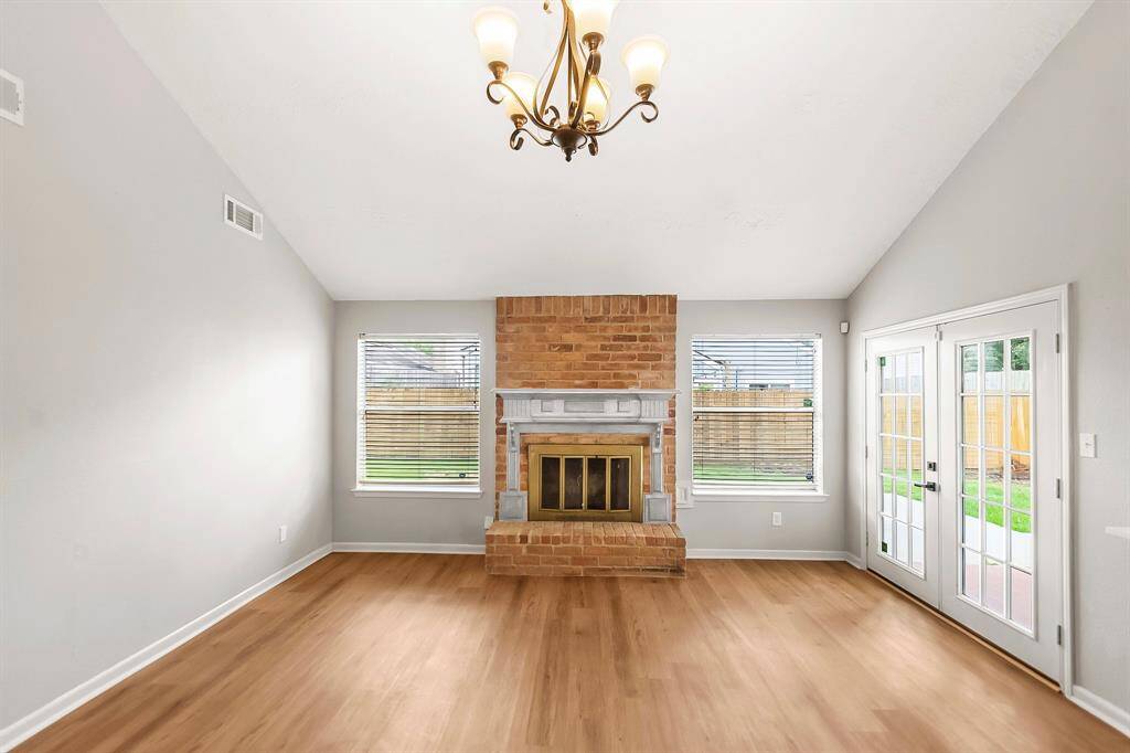 The living room features a charming brick fireplace as its focal point, complemented by wood-look luxury vinyl plank flooring and fresh paint. Double French doors open to the backyard porch, filling the space with natural light and offering a seamless indoor-outdoor flow.