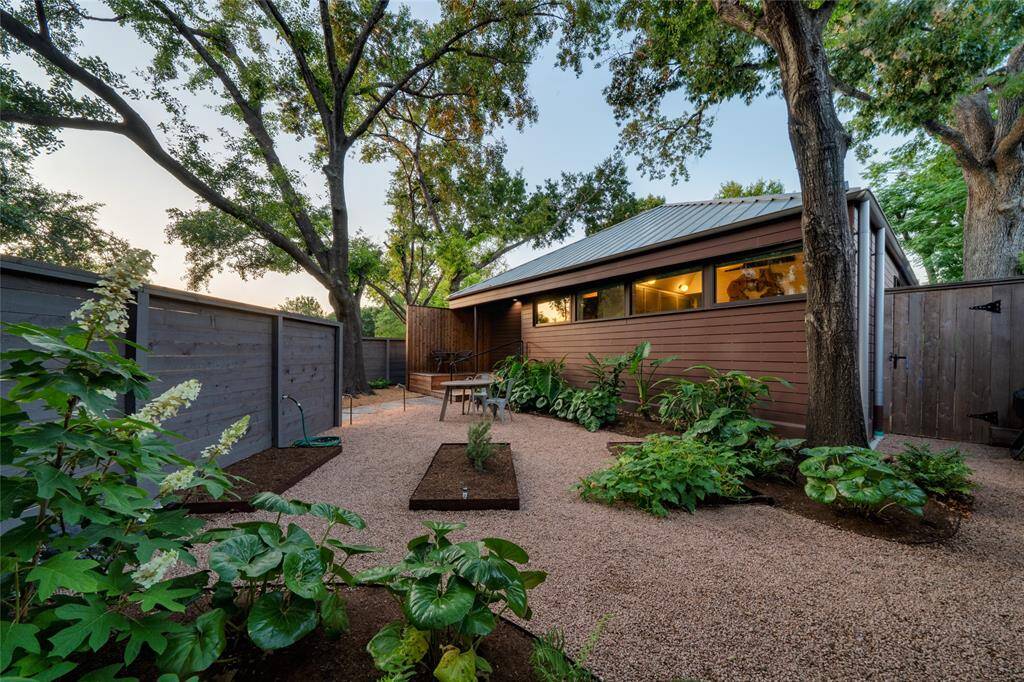 This charming front yard, nestled under a canopy of trees, features beautiful flower bays perfect for gardening enthusiasts.